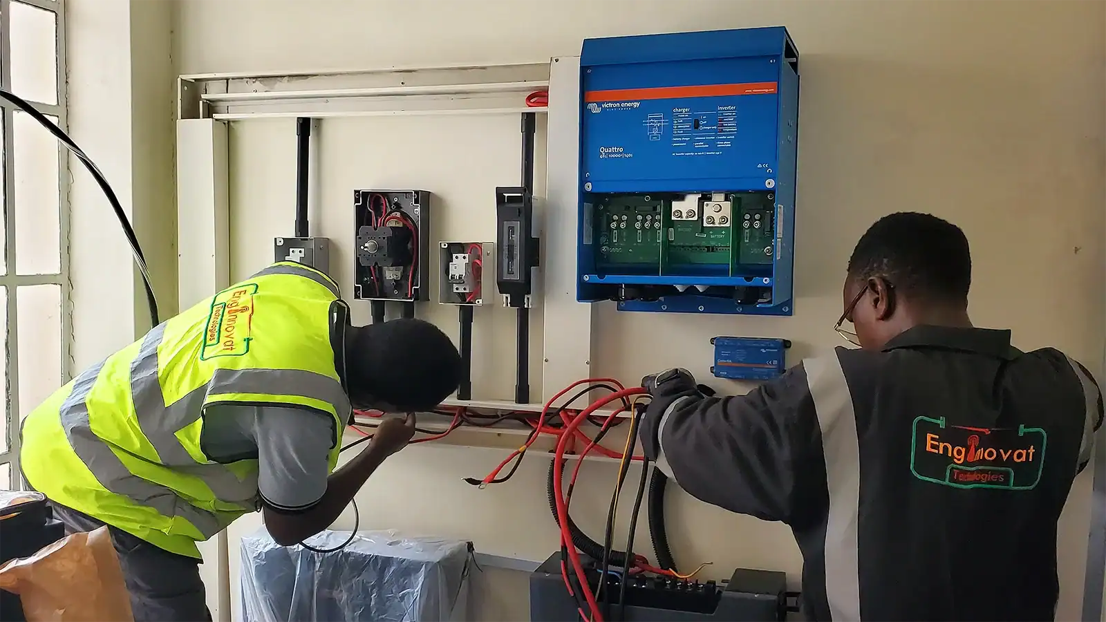 Enginnovat technicians wiring a 10 kVA Victron Quattro inverter and Weco battery backup in a campus power room.